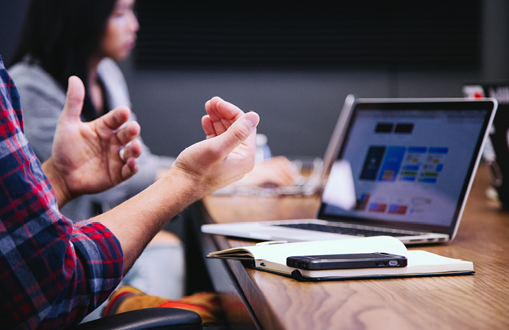 Man talking with hand motions at a table with computer.